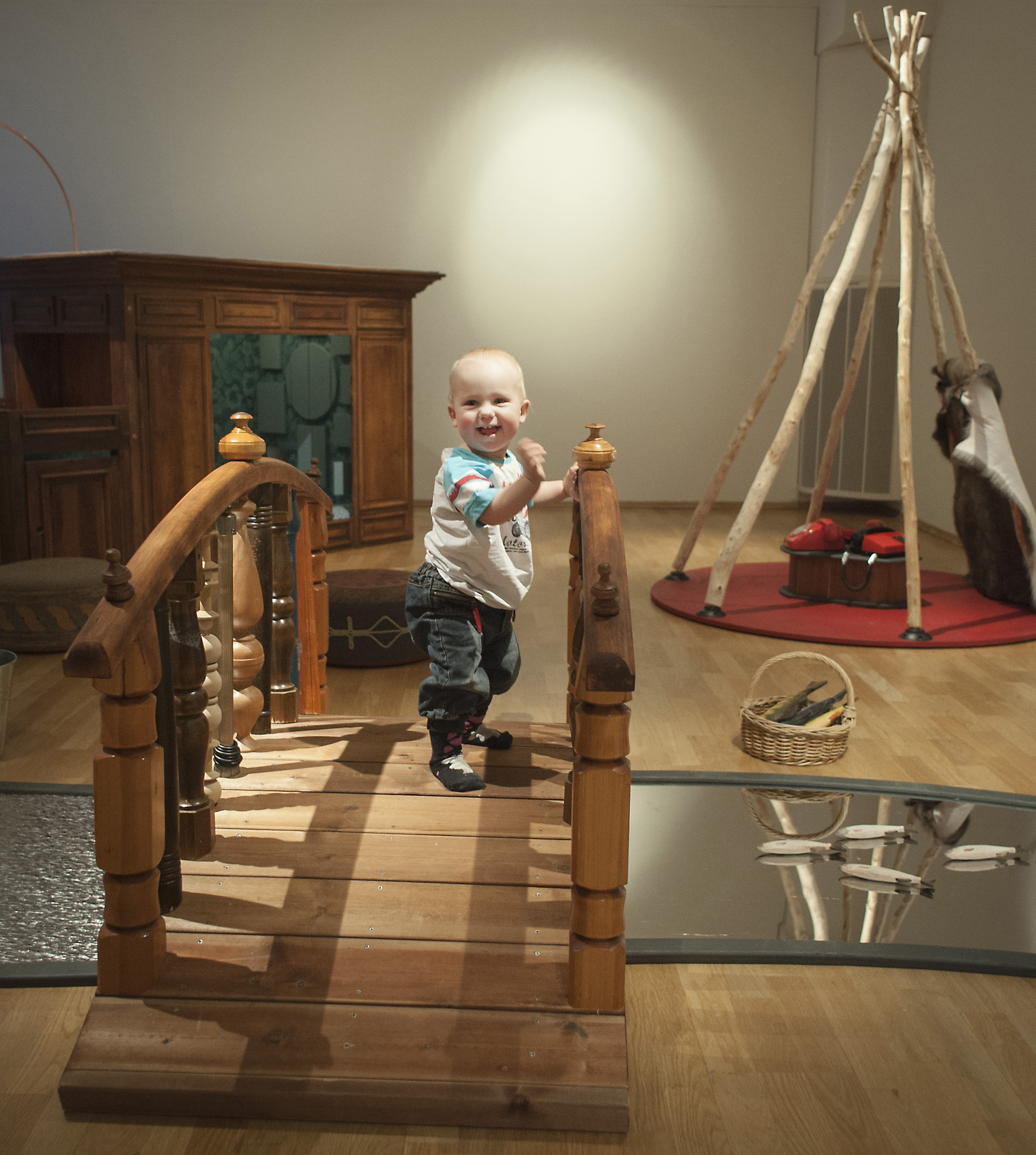 'Liten pojke som står på en bro i utställningen. Under bron flyter en älv av spegelglas, och i bakgrunden finns en kåta och en romsk vagn.'